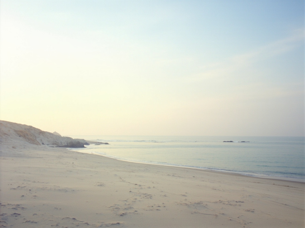 Vista ampla de uma praia tranquila ao amanhecer, com mar calmo e luz suave em tons pastel.